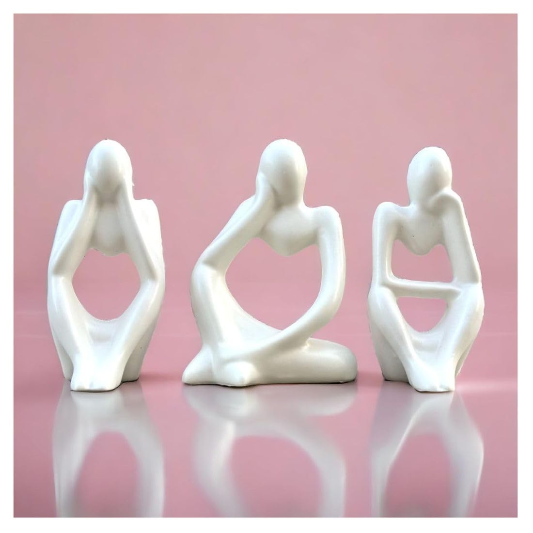 Three white ceramic figures in various poses on a pink background