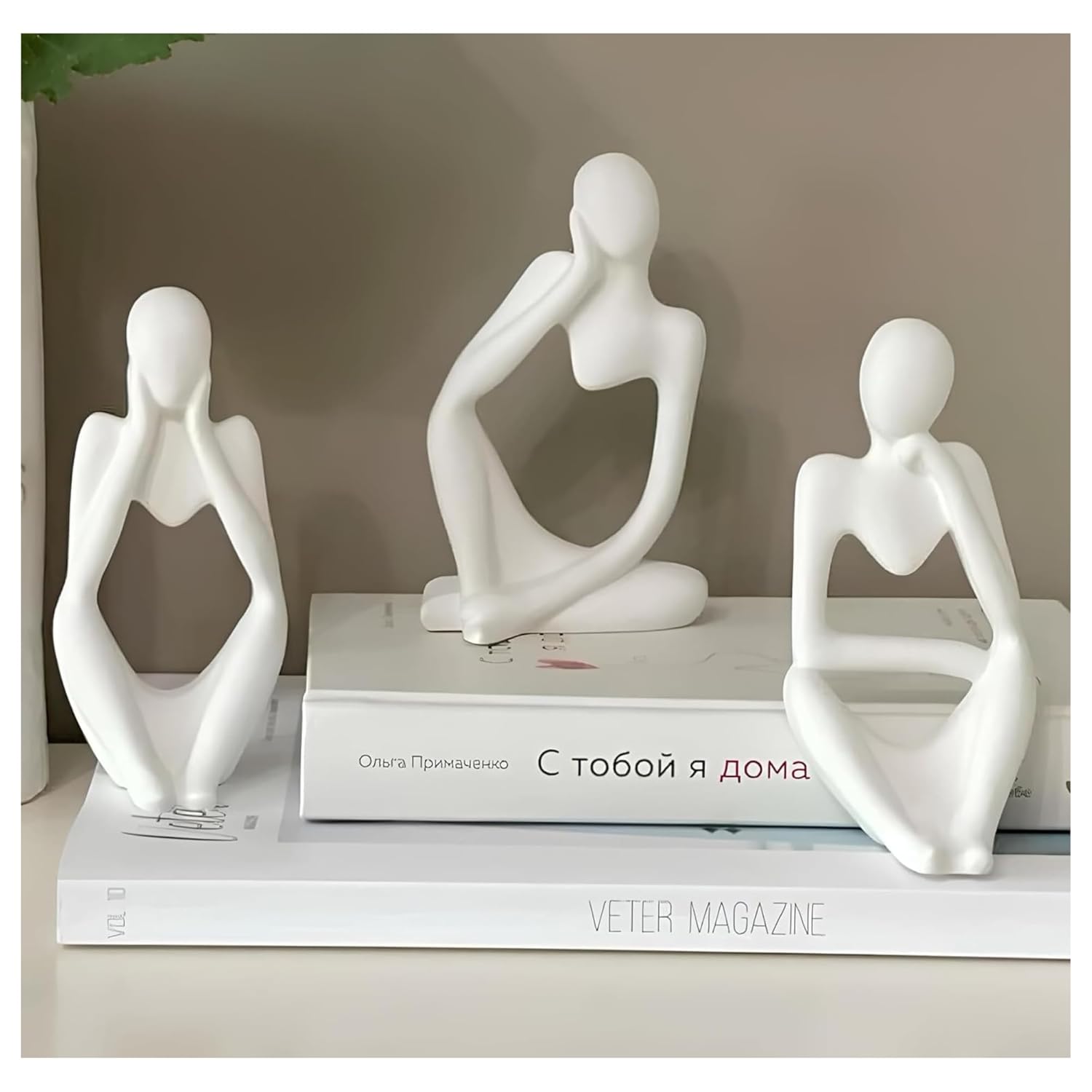 Three white abstract human-like sculptures on top of books with a neutral background