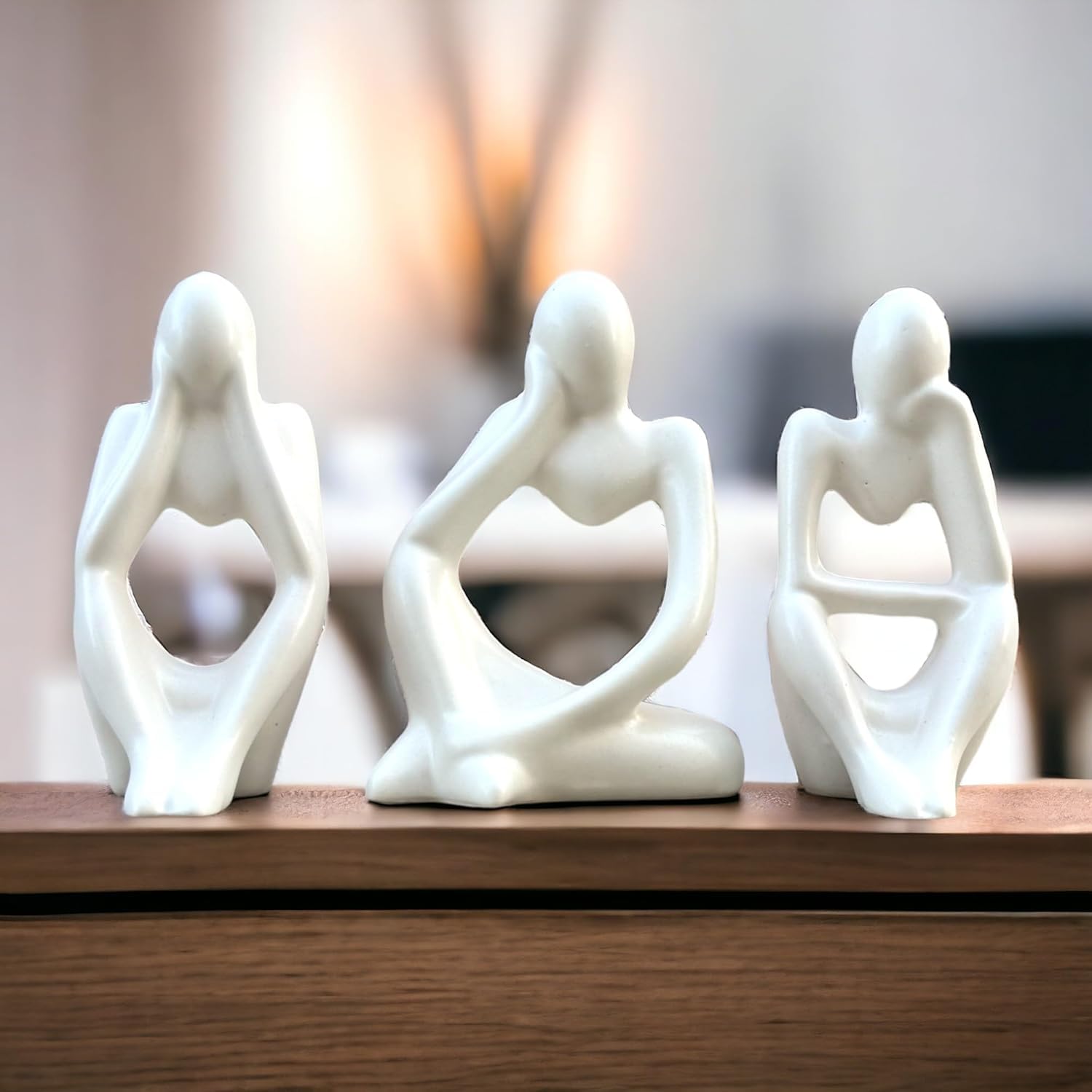 Three white ceramic figures on a wooden surface with a blurred background
