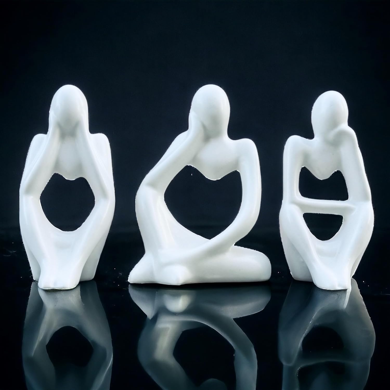 Three white ceramic figures in various poses on a reflective black surface with a dark background