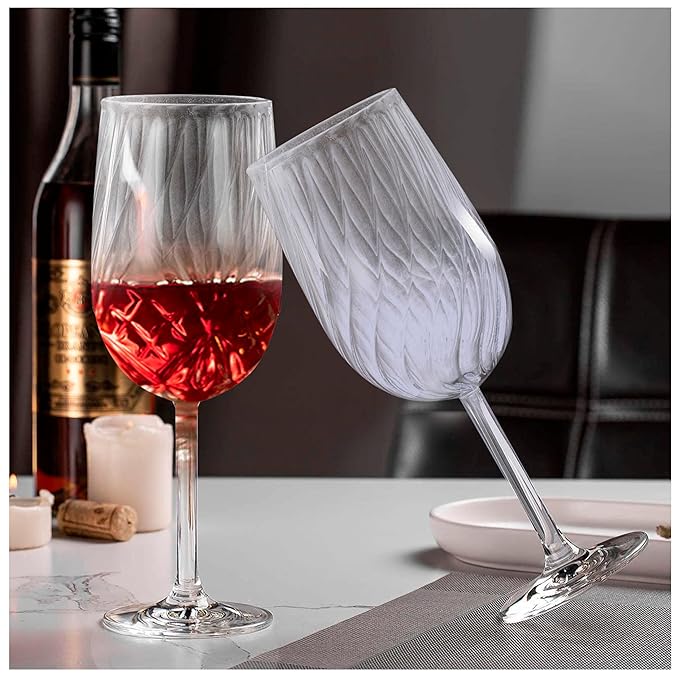 Two clear borosilicate red wine glasses, one filled with red wine, displayed on a table with a bottle and other dining accessories in the background.